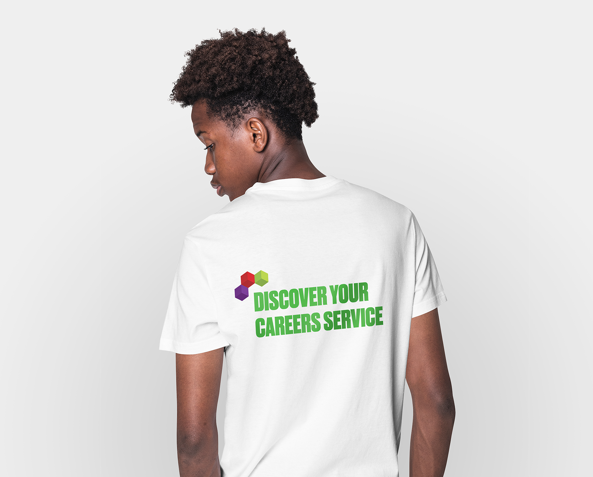 A young, Black male stands facing away from the camera. He wears a white t-shirt with the words 'Discover your careers service' on the back.